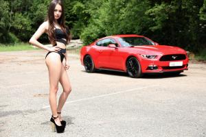 Симпатичная милая девушка позирует на фоне красного Ford Mustang